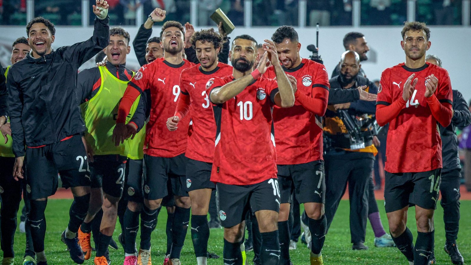 لاعبو كرة القدم المصريون يرتدون القمصان الحمراء يحتفلون بانتصار، ويقود محمد صلاح (10) التصفيق، وسط حشد متحمس.