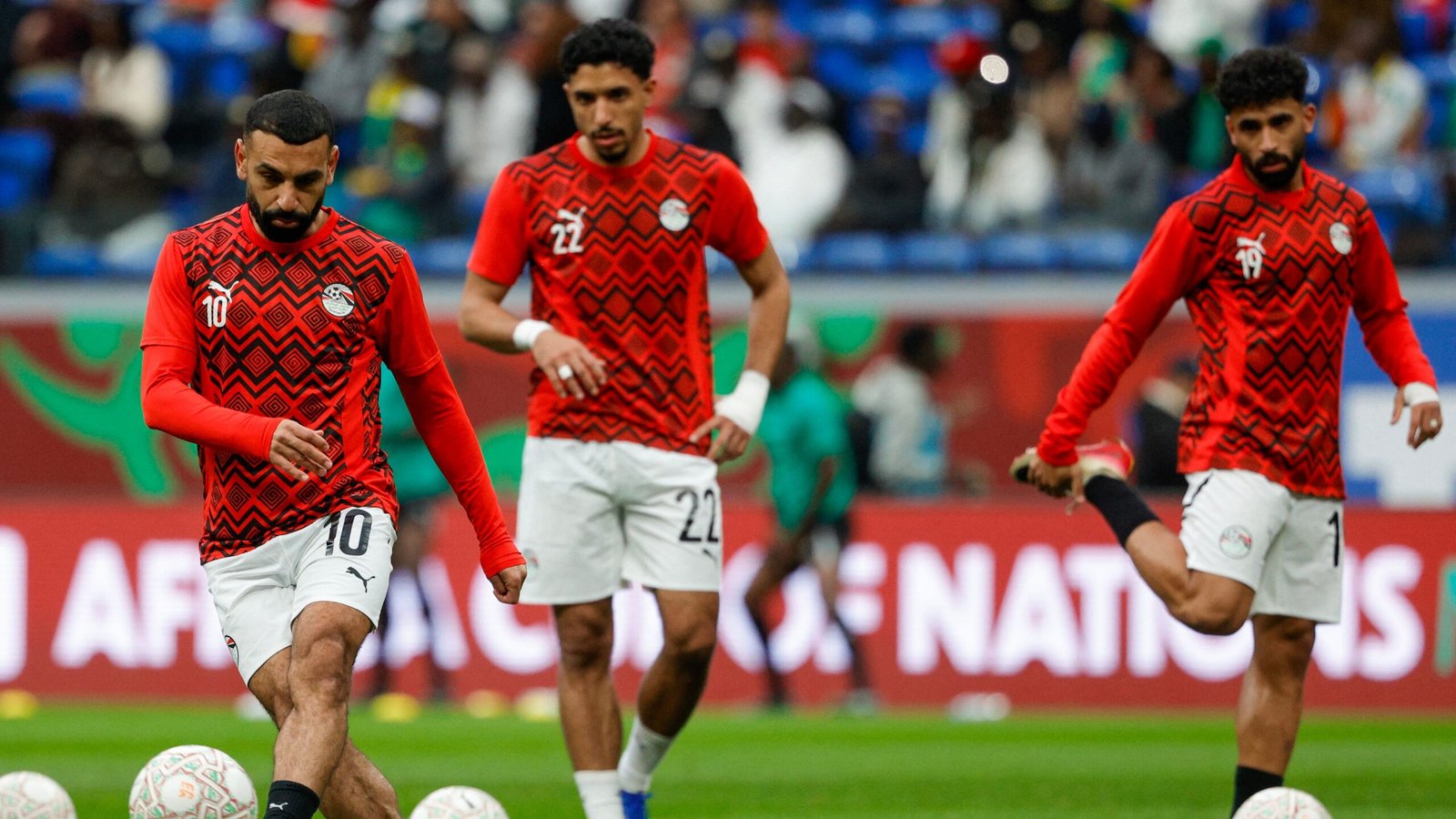 Egyptian players, including number 10, warm up in vibrant red kits with geometric patterns ahead of an Africa Cup of Nations match.