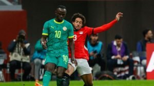 Sadio Mané in Senegal's green kit, evading an Egyptian defender during a tense match, showcasing intense competitive spirit.