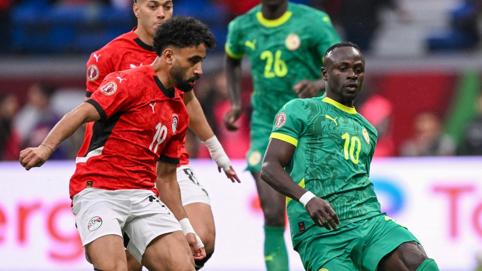 Egypt's player in red, number 18, contests the ball against Senegal's Sadio Mané in vibrant green, during a tense match moment.