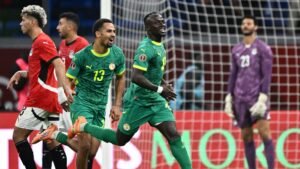 Les joueurs sénégalais célèbrent un but, portant des maillots vert vif avec des accents jaunes, tandis que l'équipe d'Égypte réagit en rouge.