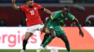Mohamed Salah in Egypt's red kit battles for the ball against a Senegalese player in green during a tense AFCON match.
