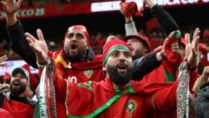Moroccan fans passionately celebrating in vibrant red and green attire during an Africa Cup of Nations match, showcasing national pride and excitement.