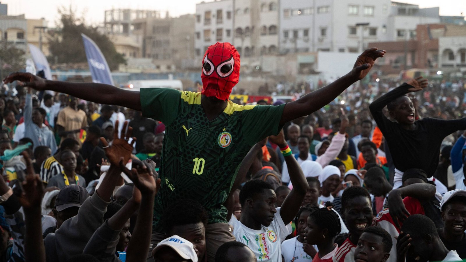 Les supporters sénégalais célèbrent avec enthousiasme, dont un fan portant un masque de Spider-Man et un maillot de l'équipe nationale.