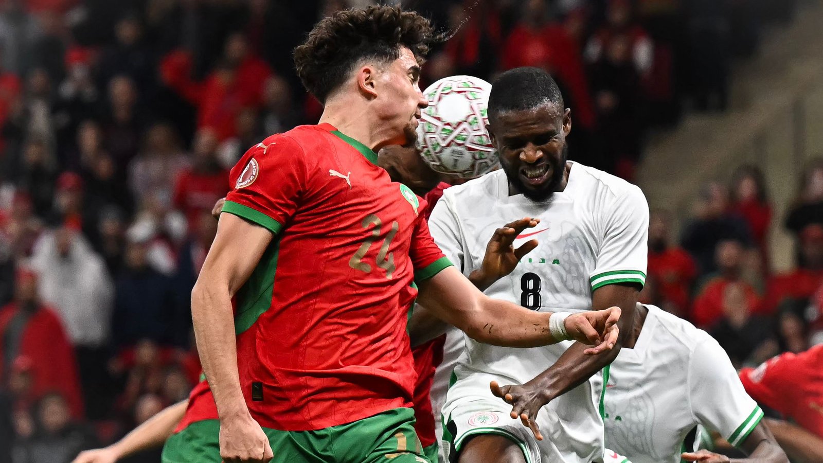 يتعارك لاعب مغربي بالزي الأحمر مع خصم باللونين الأخضر والأبيض خلال لحظة مشحونة في المباراة، مُظهرًا العزيمة والتركيز.