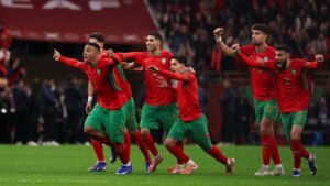 Moroccan players in red and green kits celebrate joyfully after a goal, showcasing teamwork and passion during a crucial match.