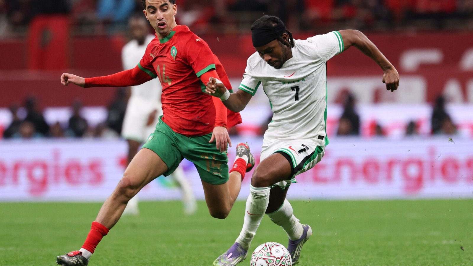 Morocco's player in red, #14, challenges an opponent in white, #7, during an intense moment of play on the pitch.