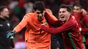 Moroccan players celebrate with goalkeeper Yassine Bounou after a victory, wearing red and green kits, showcasing team spirit and joy.