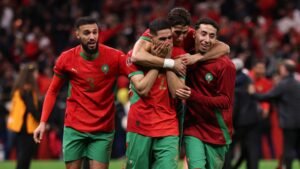 Morocco players celebrate passionately, wearing vibrant red kits with green accents, showcasing joy after a significant victory.