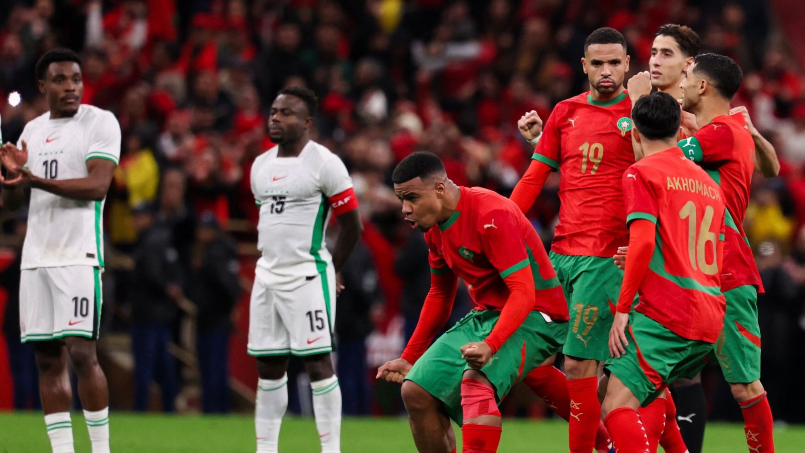 Les joueurs marocains célèbrent un but dans leur tenue rouge et vert éclatante, contrastant avec la tenue blanche de l'équipe nigériane dans une scène de match palpitante.