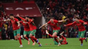 Moroccan players celebrate joyfully in vibrant red and green kits after a crucial victory, showcasing team spirit and excitement on the pitch.