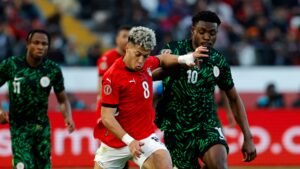 Moroccan player in a red jersey (number 8) competes for the ball against two Nigerian players in green kits during a tense match.