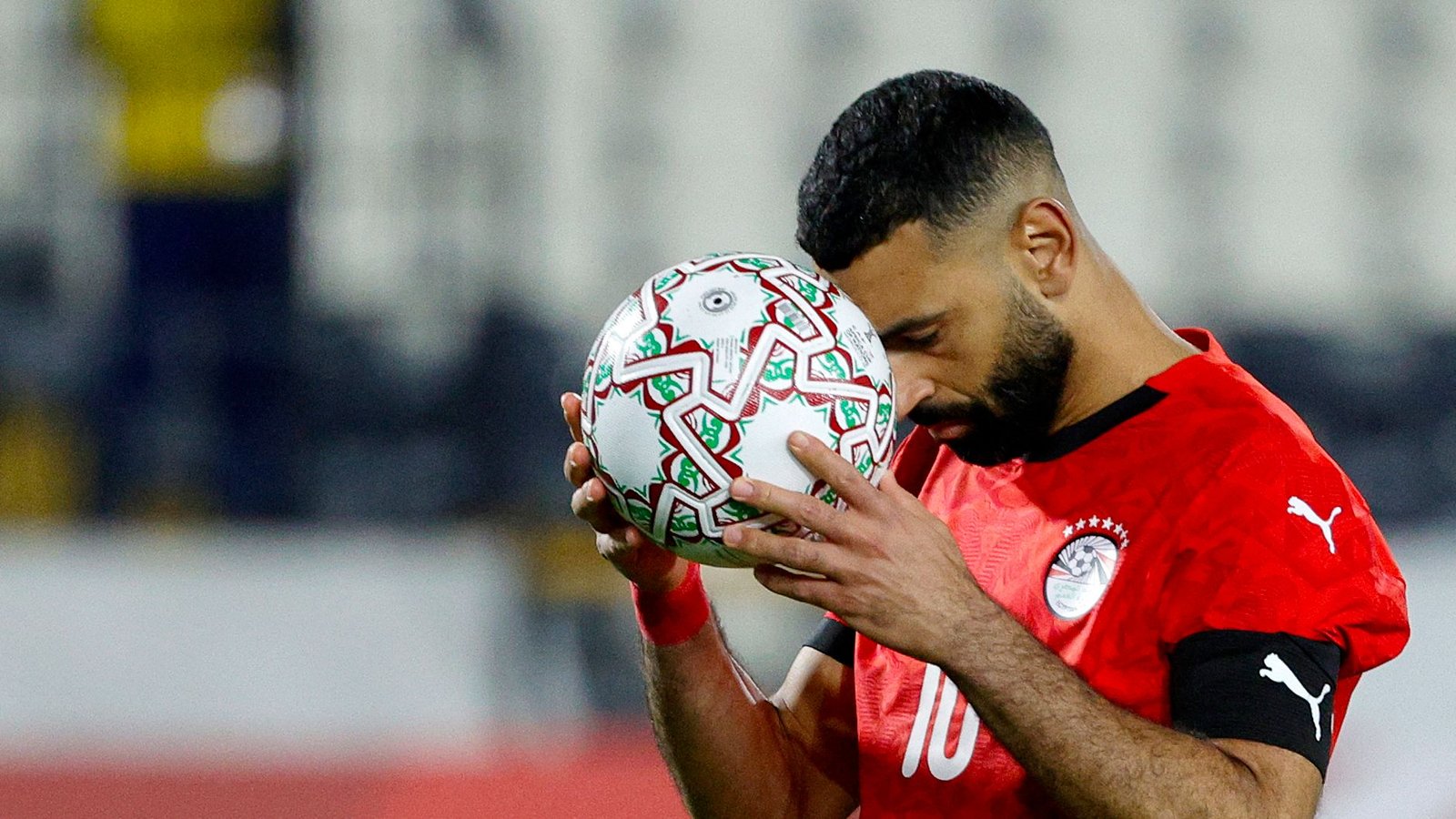 Mohamed Salah, en tenue rouge de l'Égypte, tient un ballon détaillé contre son front, affichant une concentration intense lors d'un moment crucial du match.