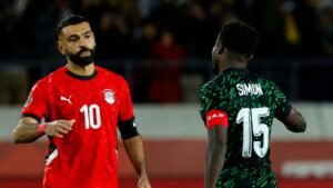 Mohamed Salah in Egypt's red kit (number 10) gestures to Nigeria's Samuel Kalu in green (number 15) during a tense match moment.
