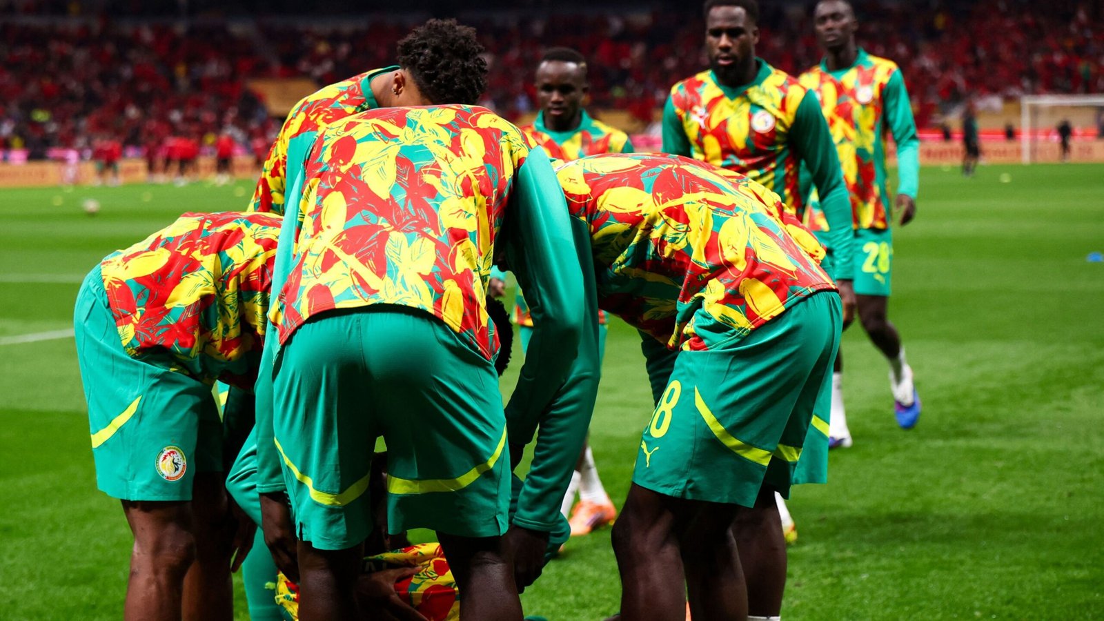 Senegalese players in vibrant green and patterned kits gather for a huddle on the pitch, showcasing team spirit in a competitive match.