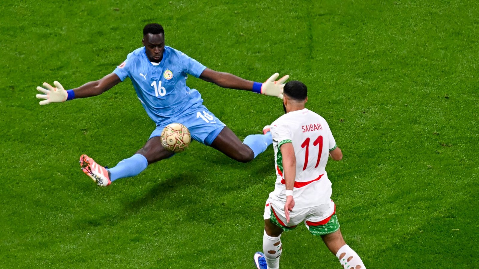 Le gardien de but sénégalais, vêtu de bleu ciel, s'étire pour arrêter un tir de Saibari du Maroc, dans un moment de tension sur le terrain.