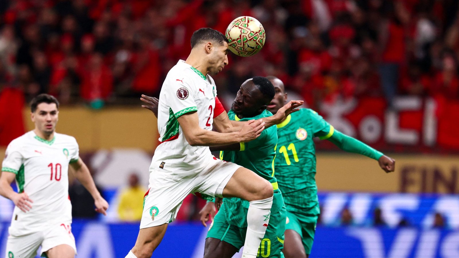 Hakimi of Morocco clashing with a Senegalese player during an intense match, with vibrant red and green fans in the background.