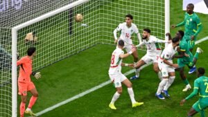 Morocco's defence scrambles as a ball approaches the goal, with players in white kits reacting during a tense moment against Senegal.