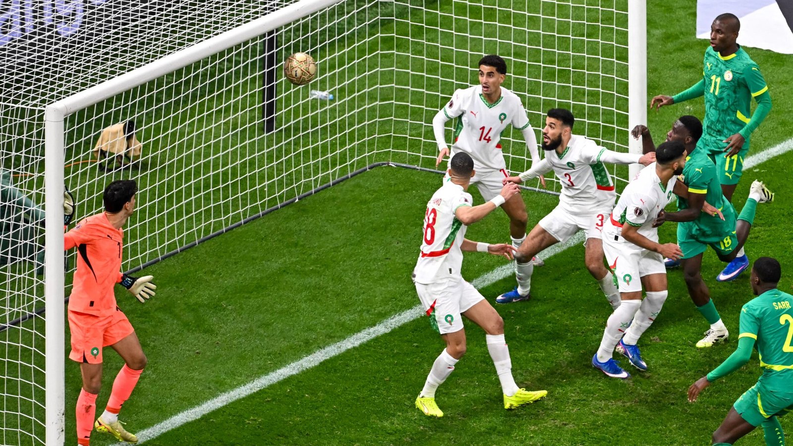 Morocco's defence scrambles as a ball approaches the goal, with players in white kits reacting during a tense moment against Senegal.
