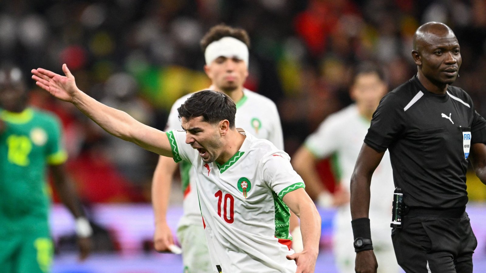 Moroccan player celebrating passionately with arms raised, wearing a white kit with green accents, during a tense match against Senegal.