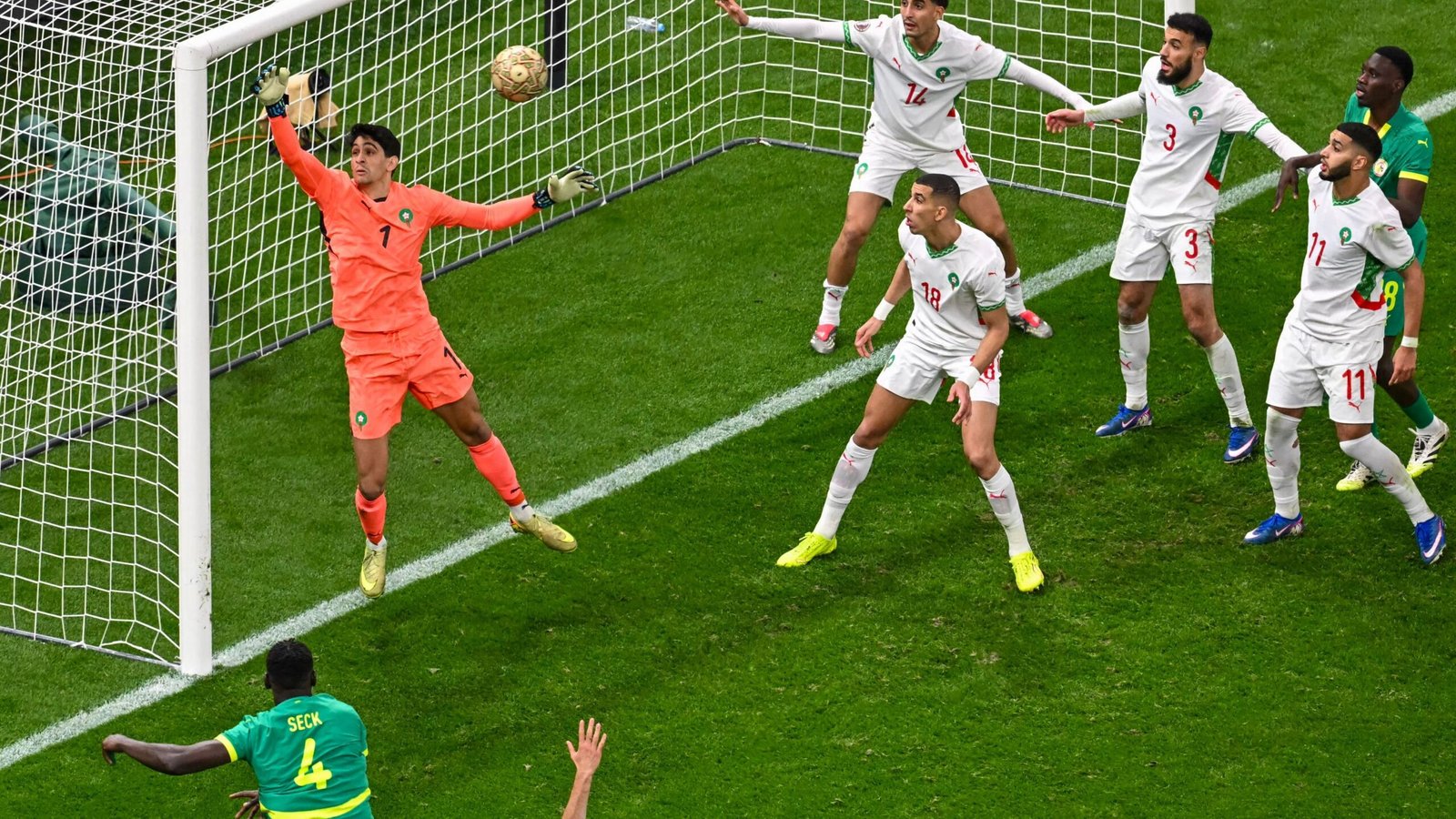 Morocco's goalkeeper makes a crucial save as teammates defend against an attacking player during a tense match scenario.
