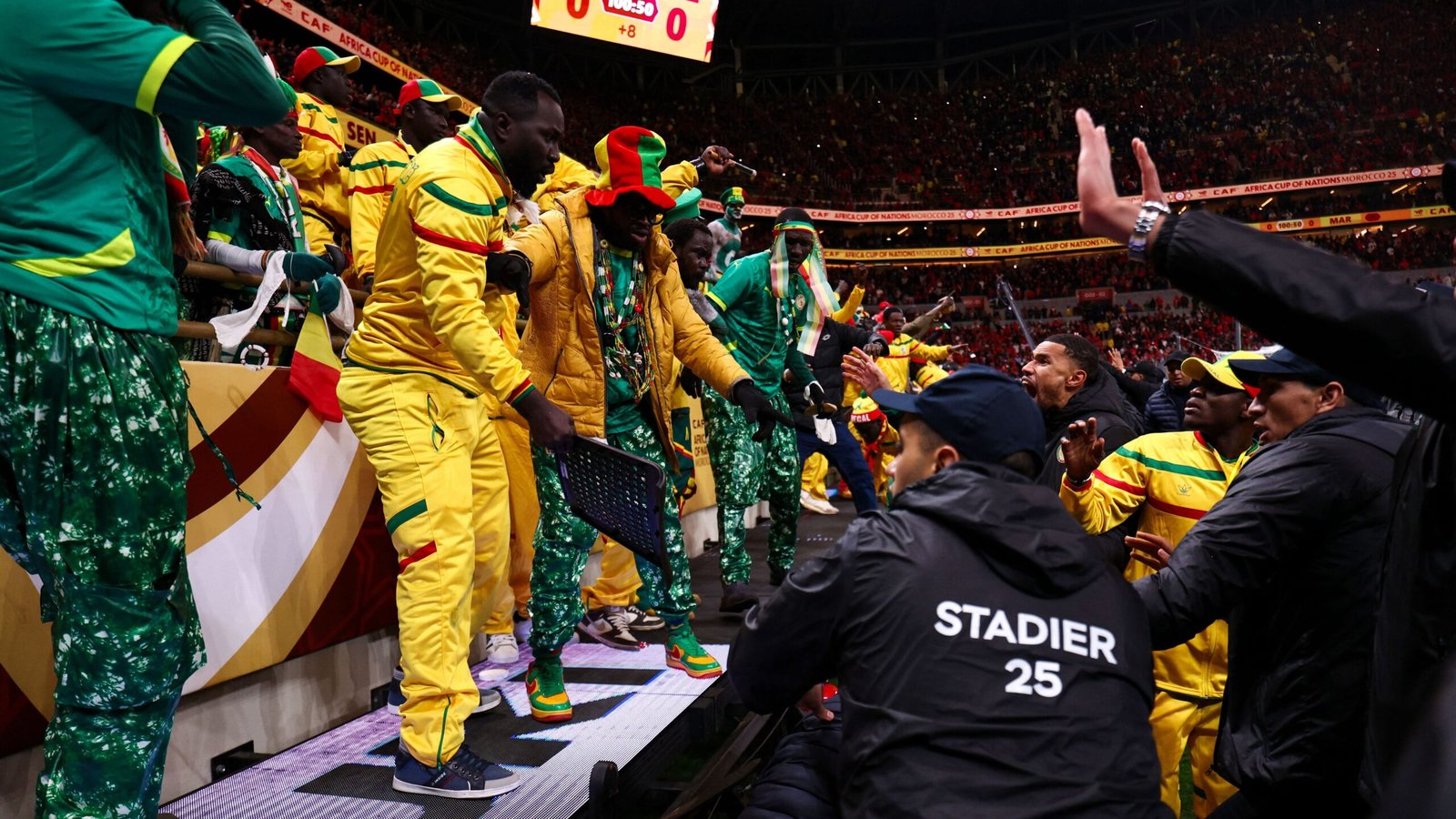 Des supporters sénégalais enthousiastes, vêtus de jaune et de vert éclatants, célèbrent en bord de terrain pendant le match de la Coupe d'Afrique des Nations, créant une atmosphère énergique.