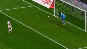 لاعب مغربي يرتدي القميص رقم 10 يستعد لتسديد ركلة جزاء، بينما حارس المرمى المنافس يرتدي الأزرق ويتوقع التسديدة قرب القائم.