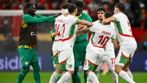 Morocco players celebrate after a goal, wearing their white and green kits, surrounded by a joyous atmosphere in the stadium.