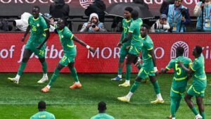 Les joueurs sénégalais, vêtus de maillots verts éclatants, célèbrent un but avec une excitation palpable, devant un fond de stade et en présence des médias.