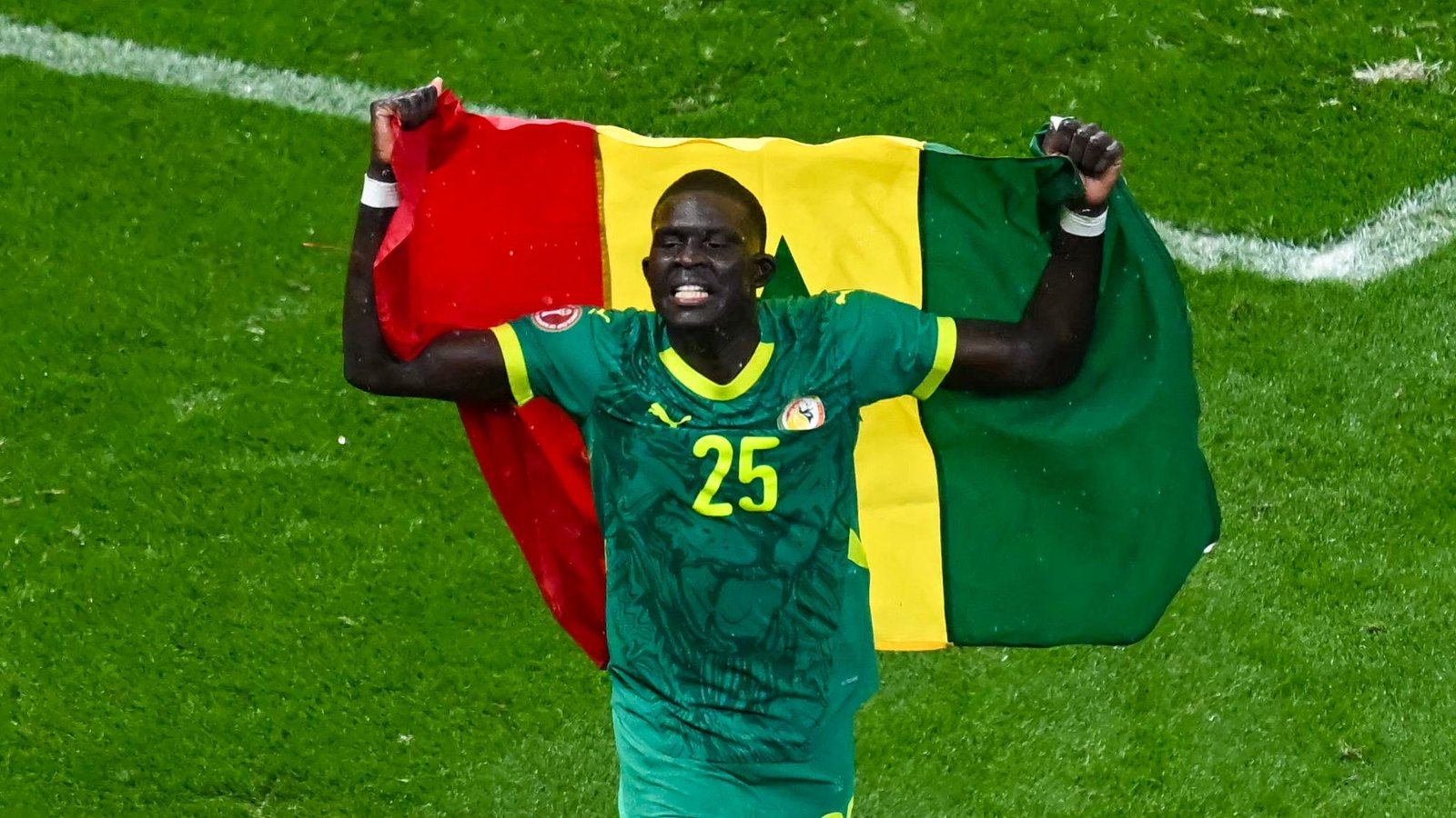 Senegalese player celebrating, holding the national flag with red, yellow, and green colours, wearing a green jersey with number 25.
