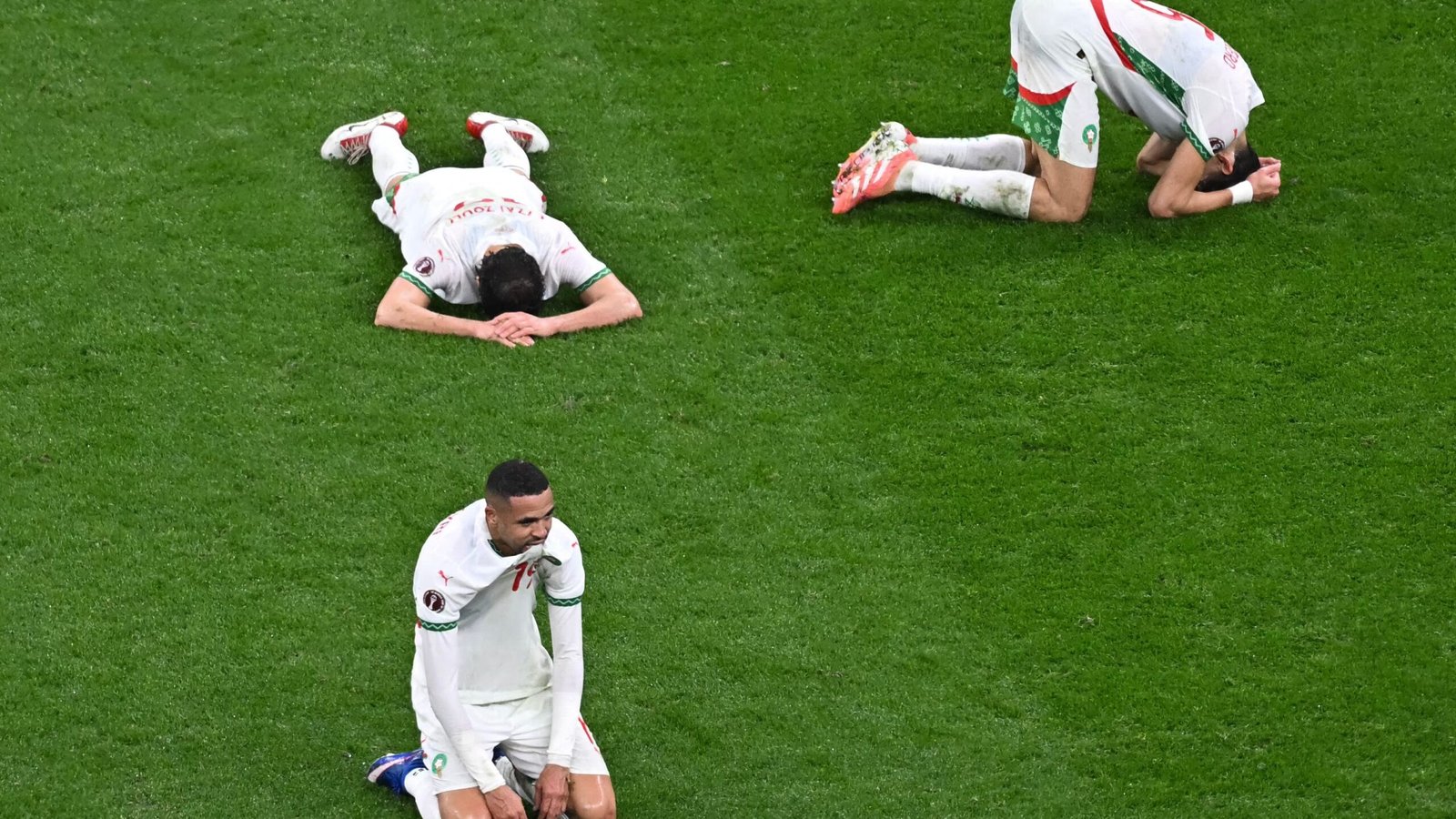 Les joueurs marocains affichent leur abattement sur le terrain, l'un agenouillé au premier plan tandis que d'autres sont allongés face contre terre sur la pelouse, reflétant leur déception.
