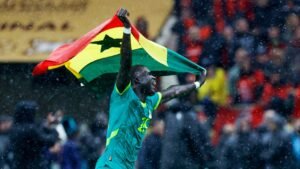 Celebrating player joyfully waves the Ghanaian flag in the rain, showcasing vibrant colours as fans cheer in the background.