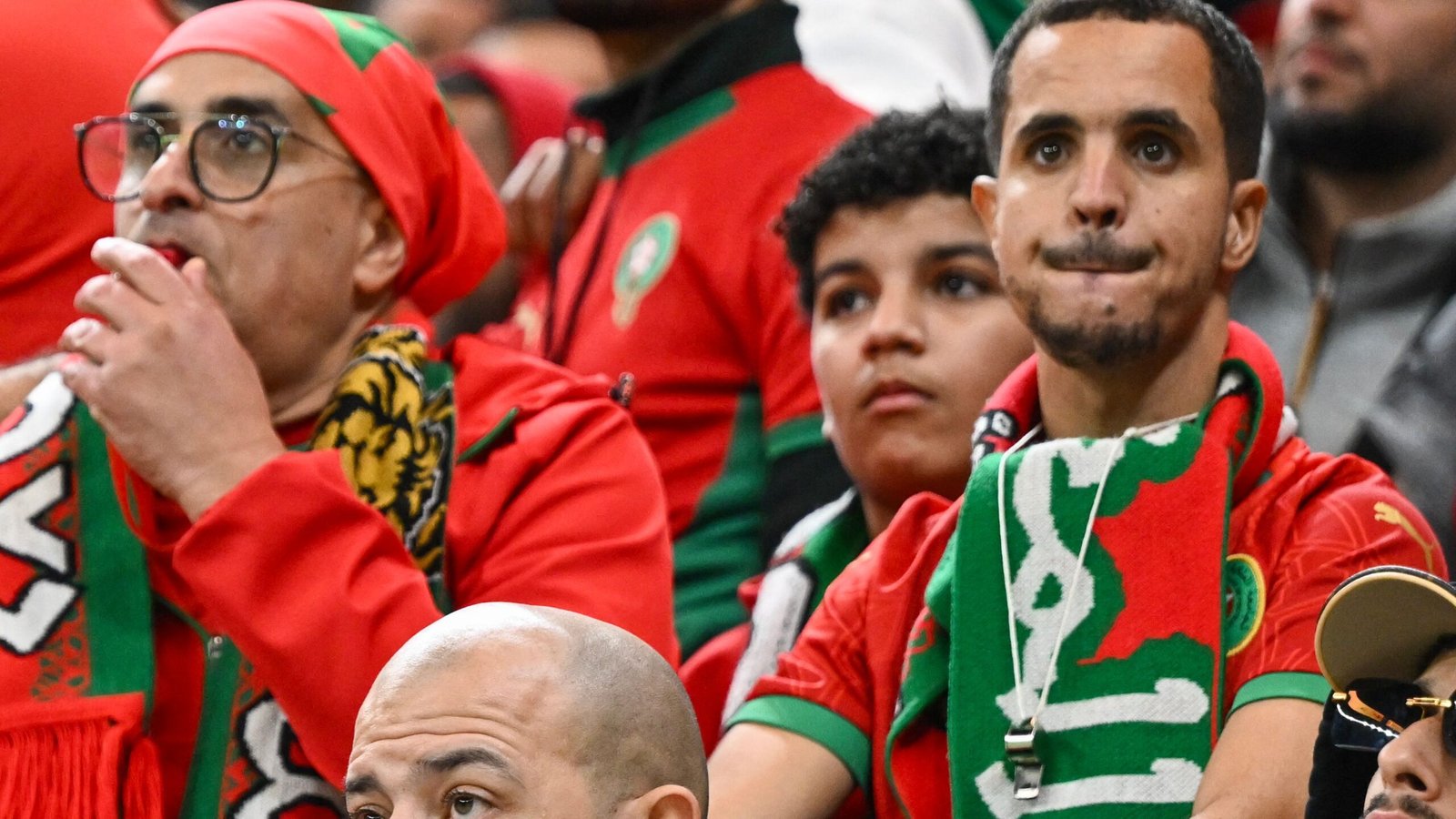 Moroccan fans in red and green attire display intense emotion, with one man holding a whistle, showing support during a match.