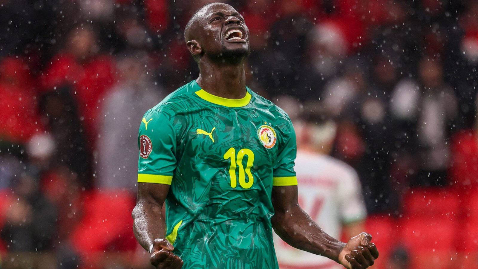 Sadio Mané célèbre avec fougue dans le maillot vert du Sénégal, sous la pluie et les acclamations de la foule.