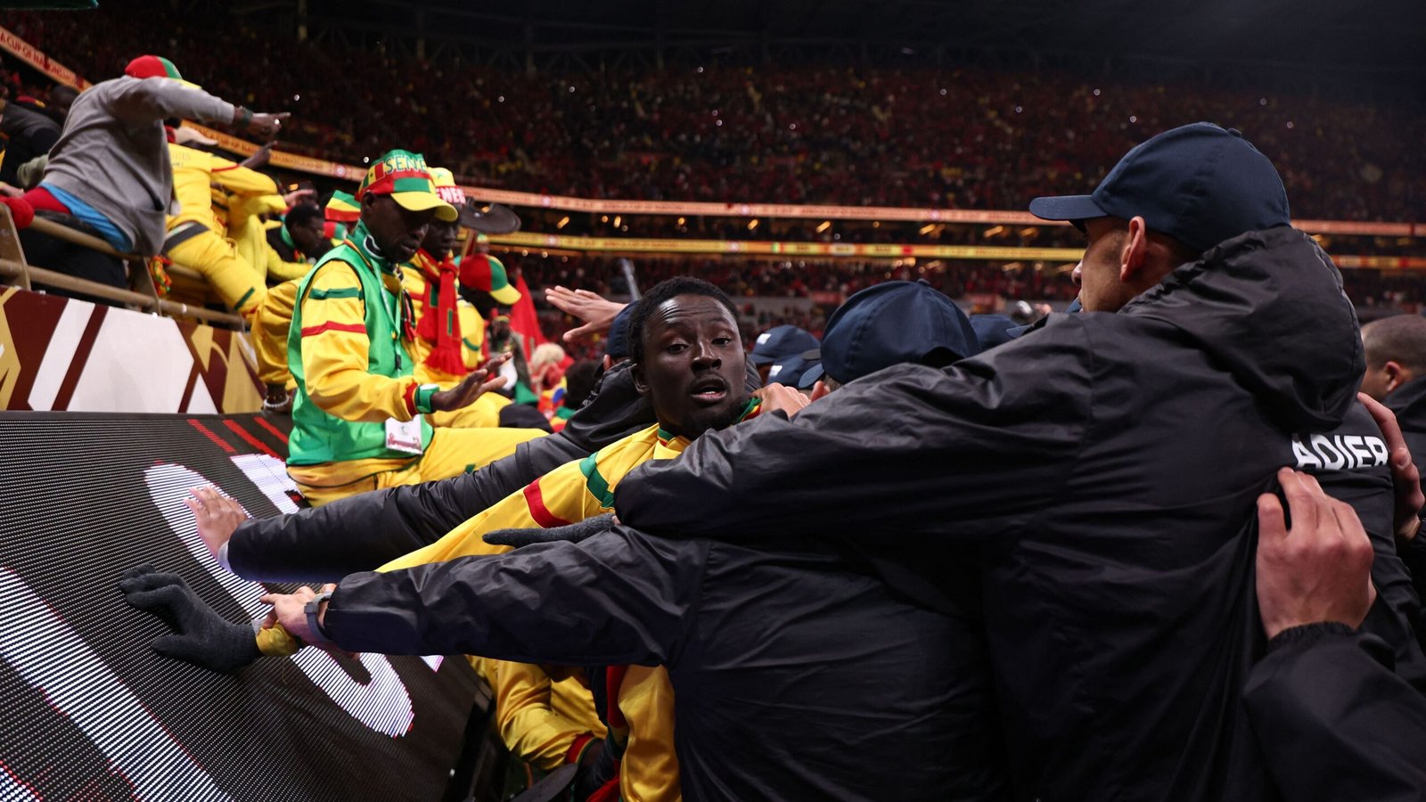 Celebrating fans in vibrant yellow and green attire, with a player in a black jacket amid the excitement in a packed stadium.