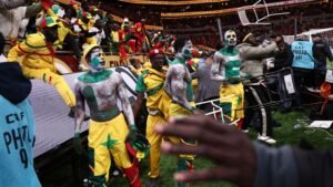 Des supporters sénégalais célèbrent, vêtus de tenues vibrantes jaunes et vertes avec des visages peints, profitant de l'ambiance de la Coupe d'Afrique des Nations.