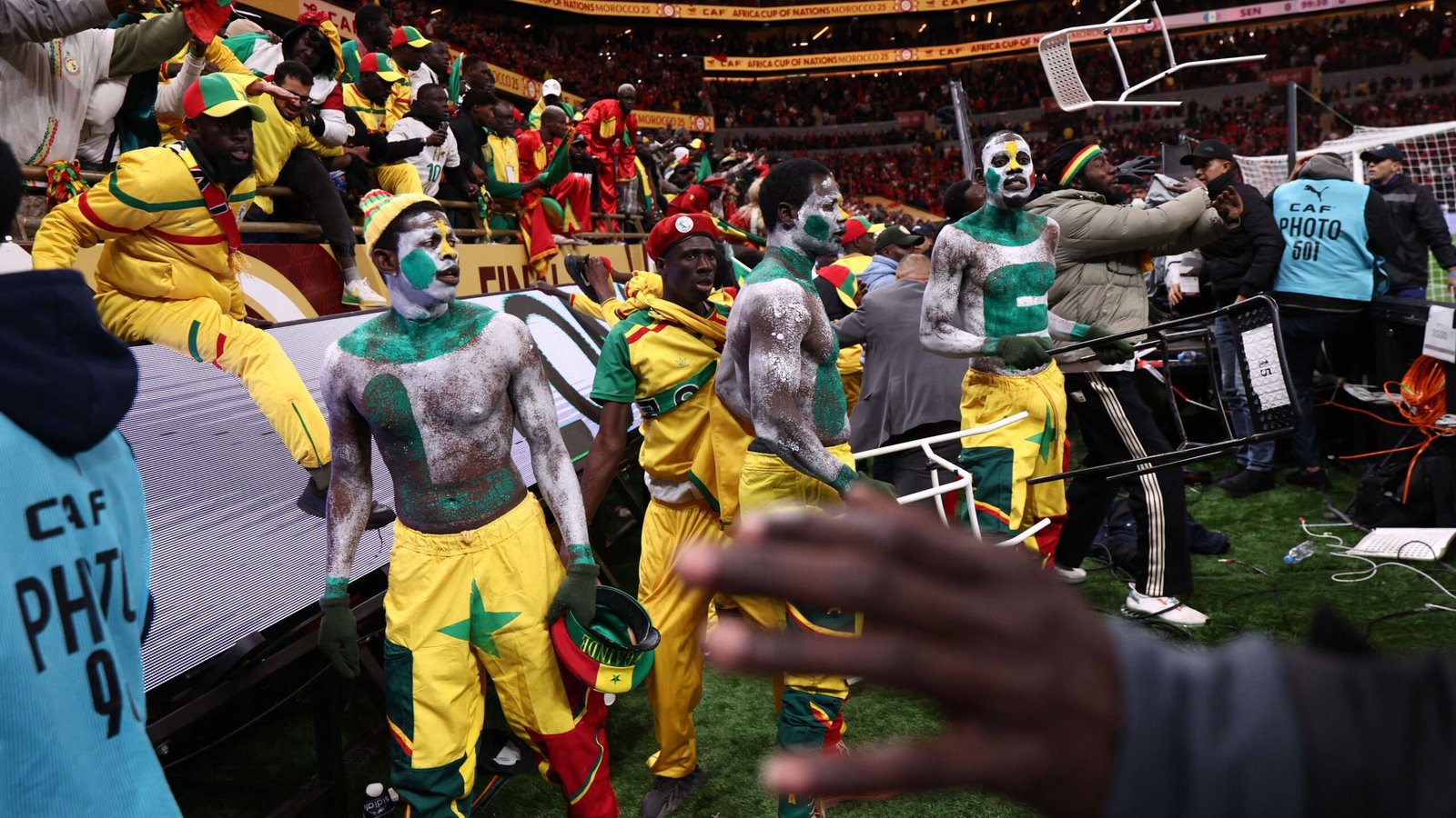 Des supporters sénégalais célèbrent, vêtus de tenues vibrantes jaunes et vertes avec des visages peints, profitant de l'ambiance de la Coupe d'Afrique des Nations.