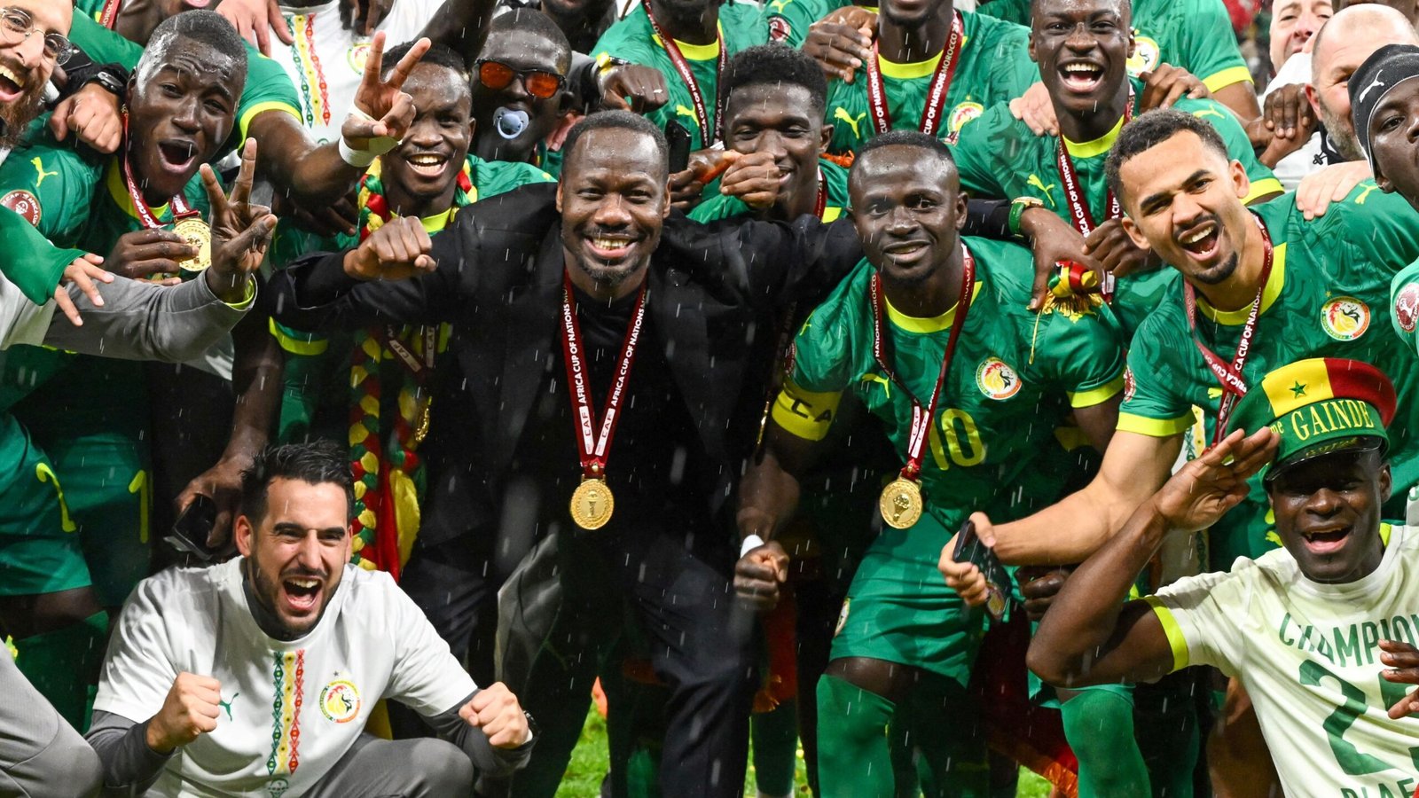Senegal's blijde spelers vieren hun Afrika Cup-overwinning, gekleed in groene tenues en gouden medailles, tussen confetti en regen.
