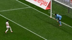 Un joueur marocain portant le numéro 10 observe tandis que le gardien de but en bleu récupère le ballon dans la surface de réparation lors d'un match intense.