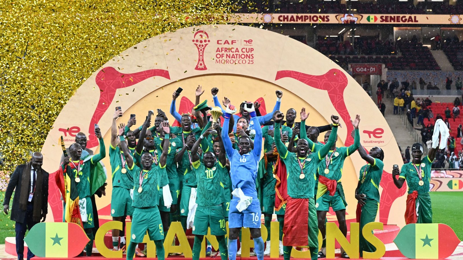 Les joueurs sénégalais célèbrent sur le podium avec le trophée de la Coupe d'Afrique des Nations, parés de médailles et entourés de confettis, après leur victoire dans le tournoi.