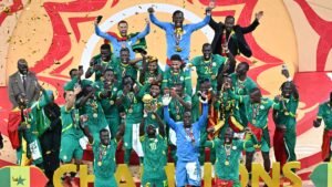 Les joueurs sénégalais célèbrent leur victoire en Coupe d'Afrique des Nations, brandissant le trophée, tandis qu'une pluie de confettis dorés tombe autour d'eux.