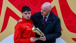 Moroccan player receiving a golden boot trophy, standing under a rain-kissed backdrop, with a dignitary offering congratulations.