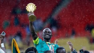 Sadio Mané brandit fièrement le trophée de la CAN, célébrant avec ses coéquipiers sous la pluie dans le stade.