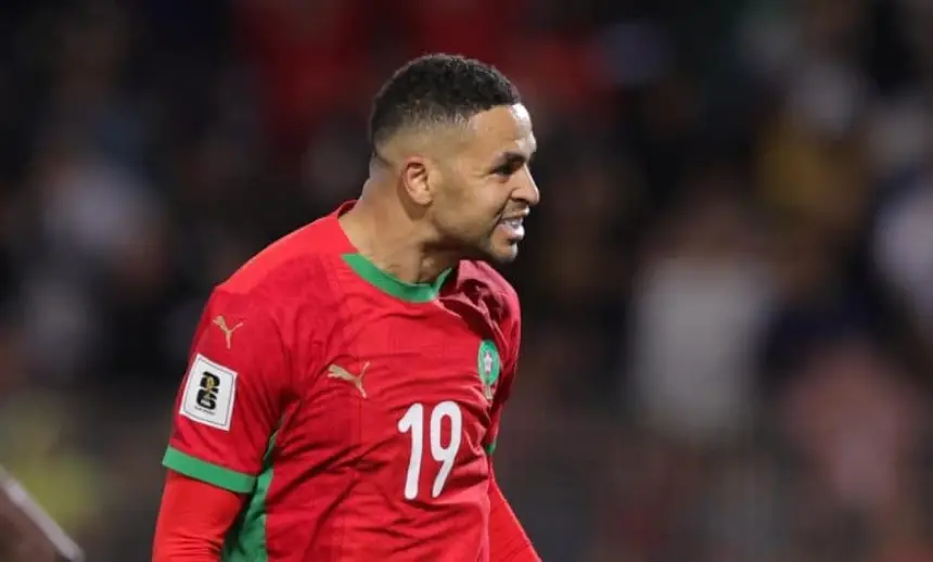 لاعب مغربي يرتدي قميصاً أحمر بلمسات خضراء ورقم 19، يحتفل بحماس بعد تسجيل هدف في أجواء ملعب مفعمة بالطاقة.