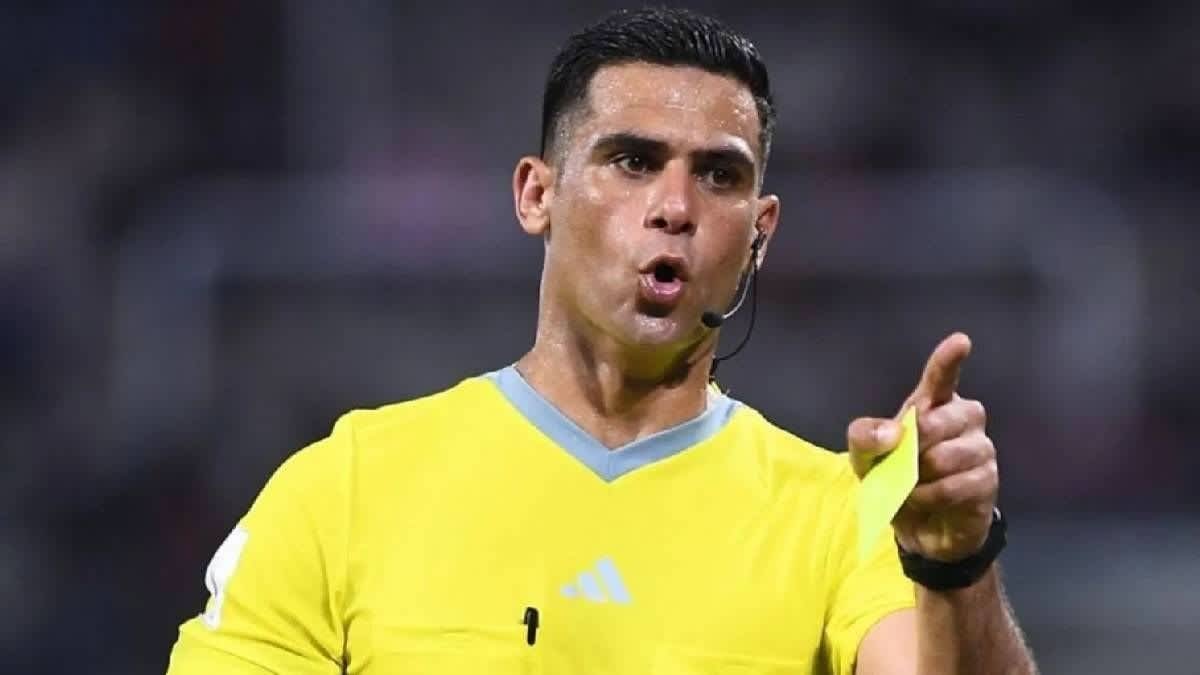 Referee in a yellow kit issues a caution with a yellow card, signalling decisively during a football match.