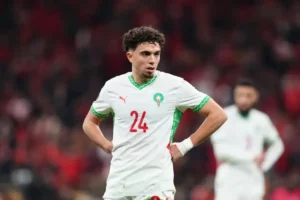 Moroccan player Neil El Aynaoui, in a white kit with green accents, looks pensive on the pitch during a tense match, jersey number 24 visible.