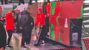 Moroccan players donning red tracksuits arrive at the stadium, with one using crutches, as they prepare for the match against their opponents.