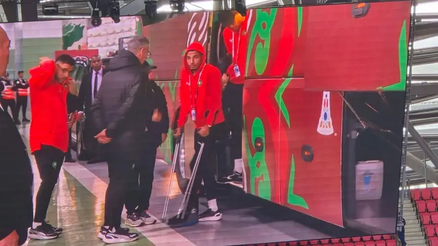 Moroccan players donning red tracksuits arrive at the stadium, with one using crutches, as they prepare for the match against their opponents.