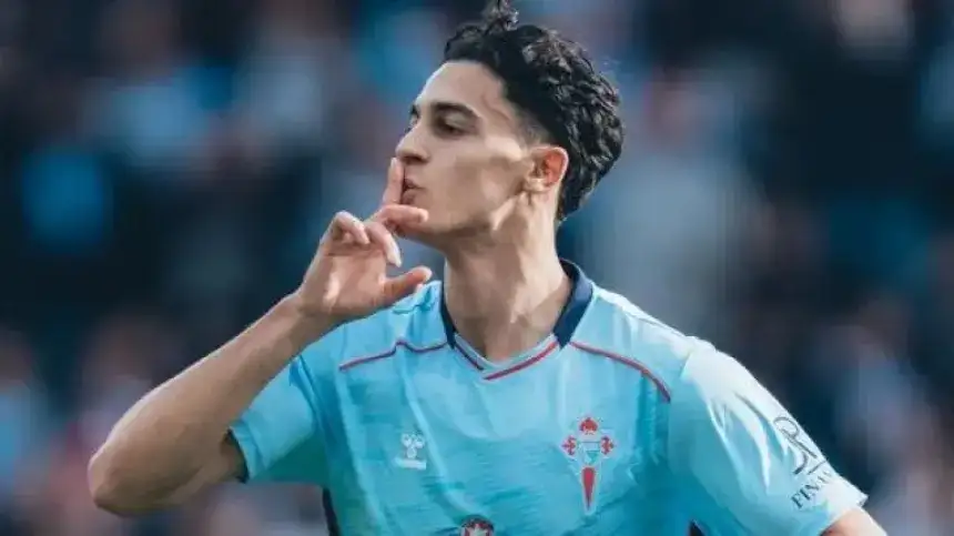 Iago Aspas celebrating a goal for Celta Vigo, wearing their light blue kit, shushing the crowd in a vibrant match atmosphere.
