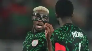 Des joueurs nigérians en maillot vert à motifs traditionnels, dont un portant un masque de protection, engagés dans une conversation animée pendant un match.